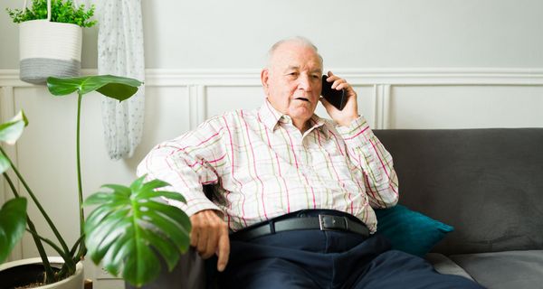 Älterer Mann, sitzt auf dem Sofa und telefoniert.