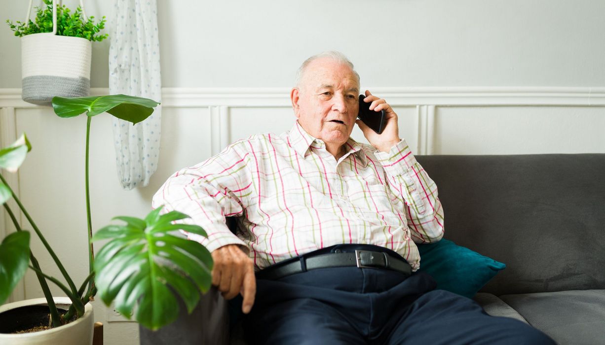 Älterer Mann, sitzt auf dem Sofa und telefoniert.