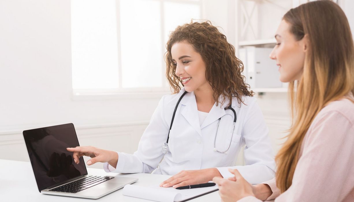 Ärztin zeigt Patientin etwas auf dem Laptop.