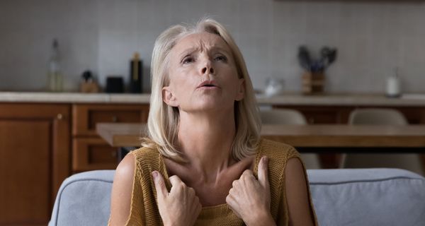 Frau, etwa 50 Jahre alt, zieht ihr Oberteil in der Nähe der Schlüsselbeine vor, um sich zu kühlen. 