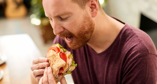 Ein Mann beißt in ein Sandwich mit Tomate, Salat und Schinken.