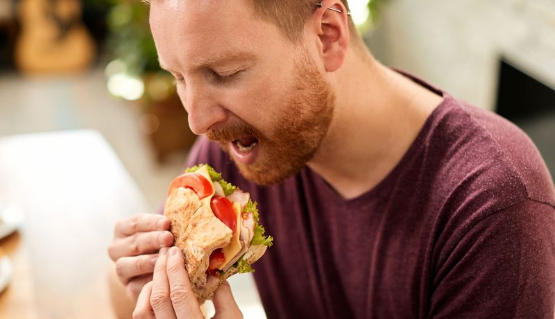 Ein Mann beißt in ein Sandwich mit Tomate, Salat und Schinken.
