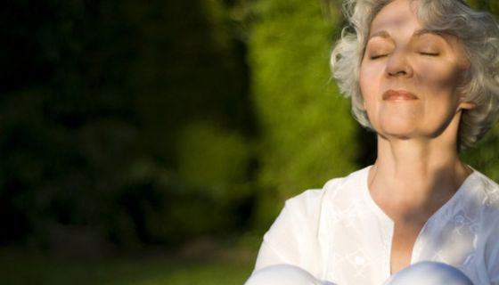 Ältere Frau sitzt im Freien in der Sonne.