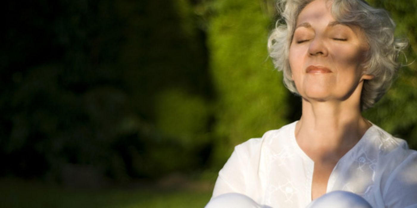 Ältere Frau sitzt mit geschlossenen Augen im Freien und genießt die Sonne