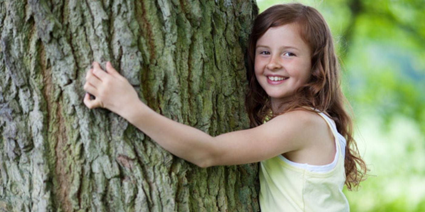 Mädchen umarmt den Stamm eines großen Baumes