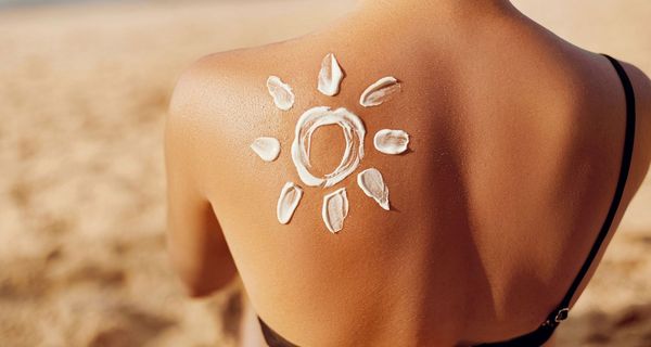 Rücken mit Sonnencreme in Form einer Sonne auf der Schulter einer jungen Ffrau.