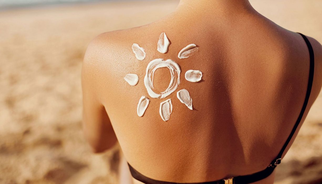 Rücken mit Sonnencreme in Form einer Sonne auf der Schulter einer jungen Ffrau.