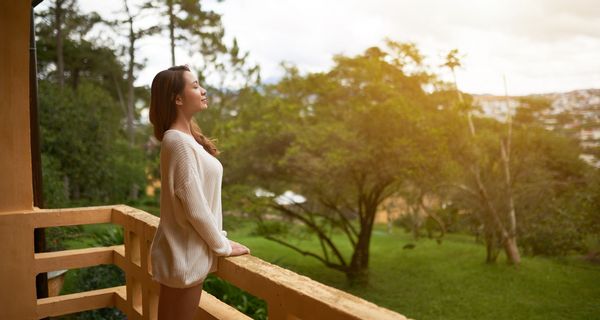 Frau, steht auf einem Balkon mit Blick ins Grüne.