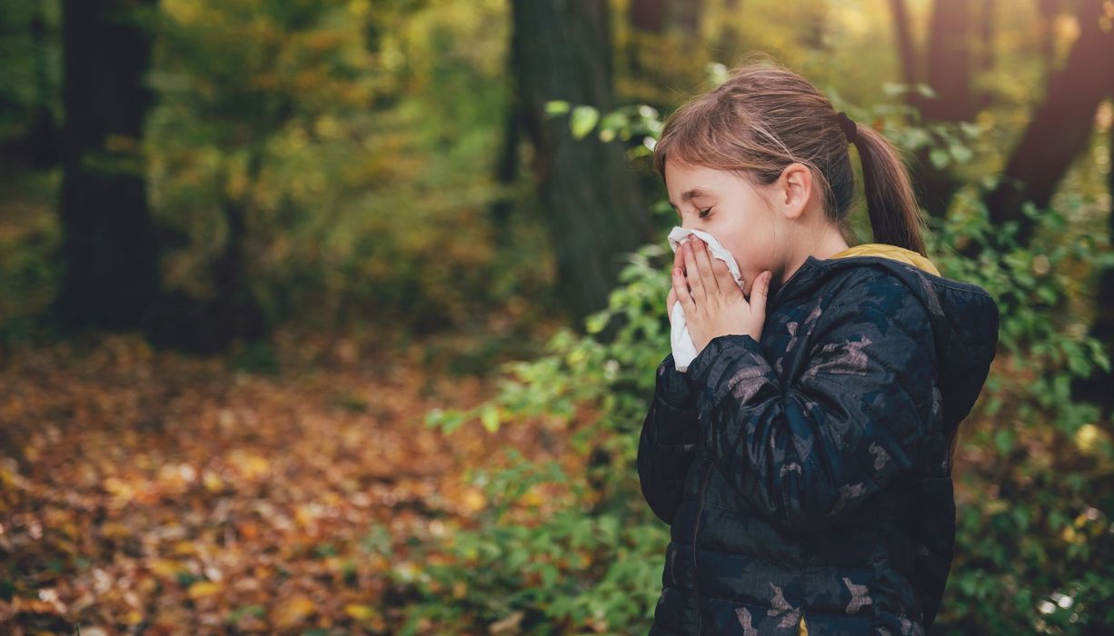 Mädchen steht in der Natur und putzt sich die Nase