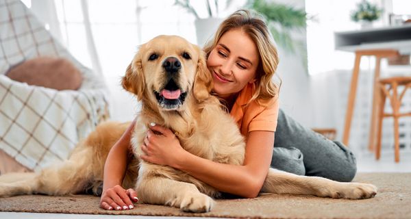 Eine Frau kuschelt mit einem Golden Retriever auf dem Teppich.