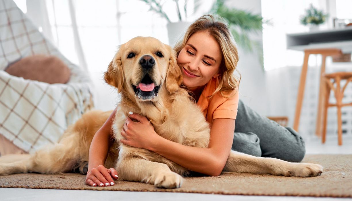 Eine Frau kuschelt mit einem Golden Retriever auf dem Teppich.