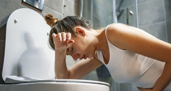 Frau beugt sich über eine Toilettenschüssel und hält sich den Bauch. Sie sieht nicht glücklich aus.