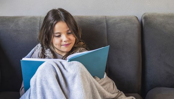 Mädchen, sitzt auf der Couch und liest ein Buch.