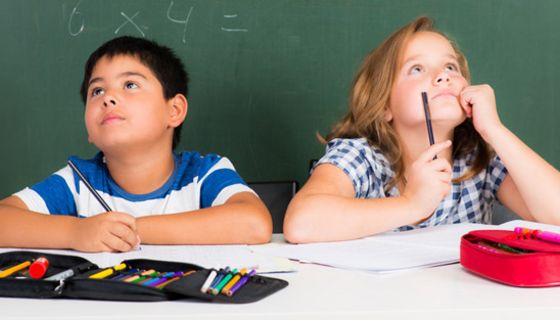 Übergewichtige Schülerin und Schüler, ca. 11 Jahre alt, im Klassenraum vor einer Wandtafel mit Matheaufgaben sitzend. Beide schauen nach oben