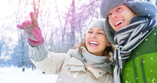 Vergnügtes Paar in winterlicher Landschaft (in den 20ern: Er grüner Anorak und Fellmütze mit Ohrenklappen, sie heller Anorak, rosa Handschuhe, hellgraue Mütze und Schal)