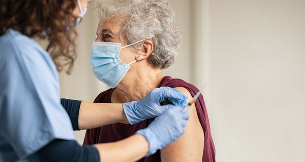 Seniorin mit Maske, wird von Ärztin geimpft.