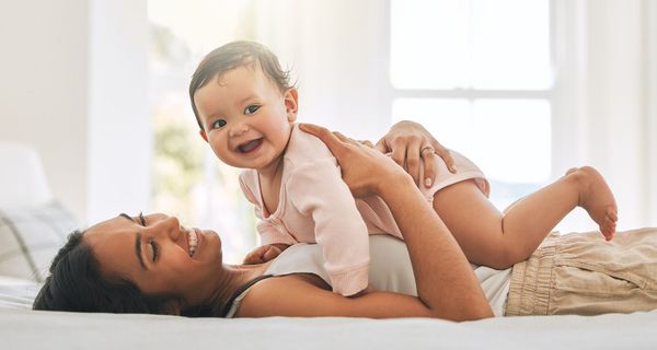 Junge Mutter spielt mit Baby im Bett.