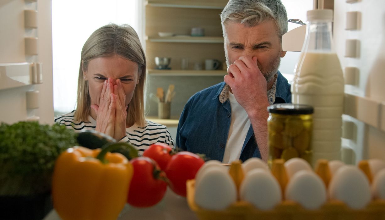 Paar steht vor offenem Kühlschrank und hält sich die Nase zu.