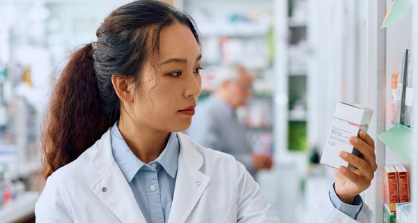 Eine Apothekerin blickt prüfend auf ein Präparat in ihrer Hand.