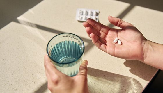 Hand mit zwei Tabletten neben Wasserglas