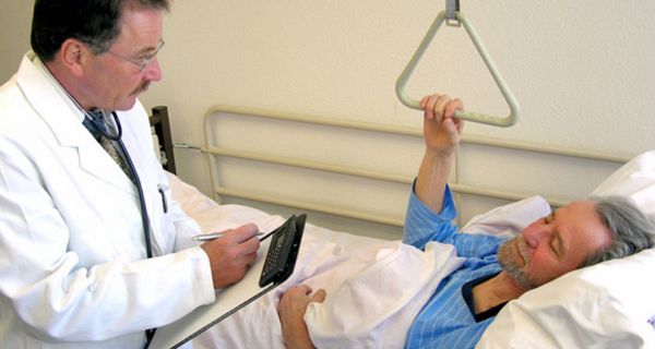 Patient im Krankenbett mit Arzt, der ein Klemmbrett mit einem Dokument in den Händen hält