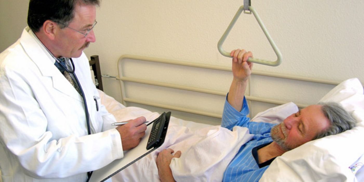 Patient im Krankenbett mit Arzt, der ein Klemmbrett mit einem Dokument in den Händen hält