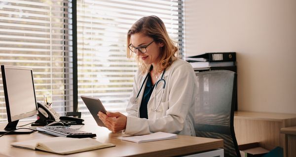 Ärztin im Behandlungszimmer mit Tablet in der Hand.