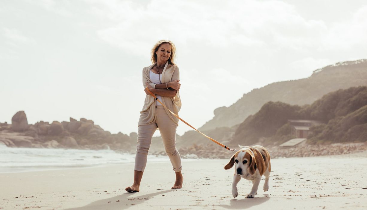 Frau, geht am Strand spazieren mit einem Hund.