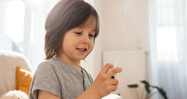 Ein Kind mit schulterlangen Haaren hält ein Nasenspray in der Hand und betätigt es.