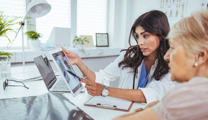 Ärztin schaut mit Patientin auf Röntgenaufnahme.