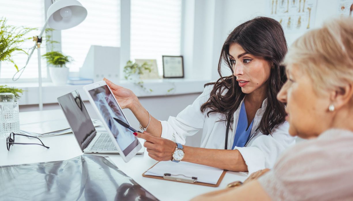 Ärztin schaut mit Patientin auf Röntgenaufnahme.