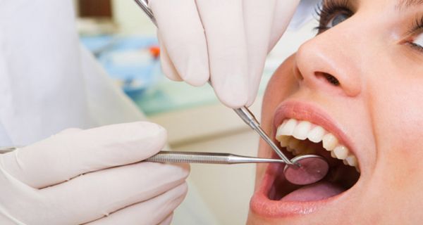 Junge Frau mit geöffnetem Mund beim Zahnarzt; vor dem Mund: Behandschuhte Hand hält Untersuchungswerkzeug