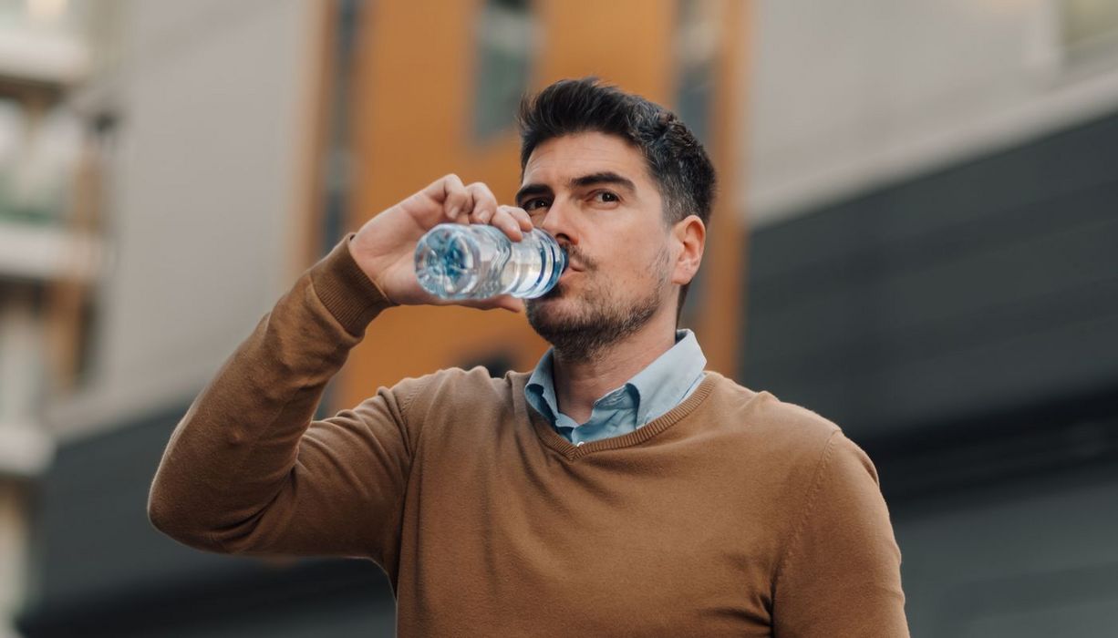 Junger Mann trinkt Wasser aus einer Plastikflasche.