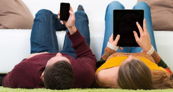 Zwei Jugendliche liegen auf dem Rücken und lesen auf Tablet und Smartphone.