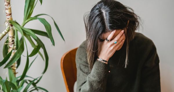 Junge dunkelhaarige Frau, verdeckt ihr Gesicht mit den Händen.