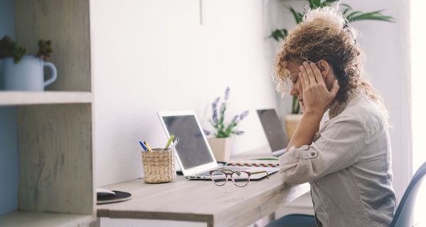 Frau mit Migräne, sitzt am Schreibtisch.
