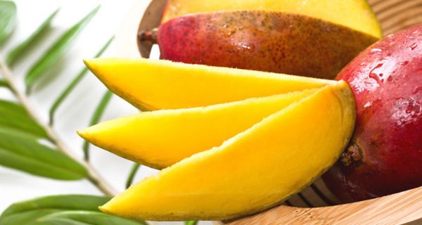 Drei Mangospalten, dahinter eine aufgeschnittene und eine ganze Mango