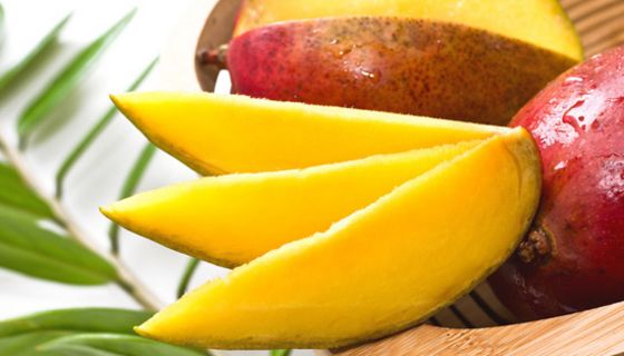 Drei Mangospalten, dahinter eine aufgeschnittene und eine ganze Mango