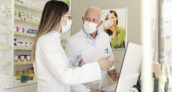 Zwei Apotheker mit Maske vor einem Computer.