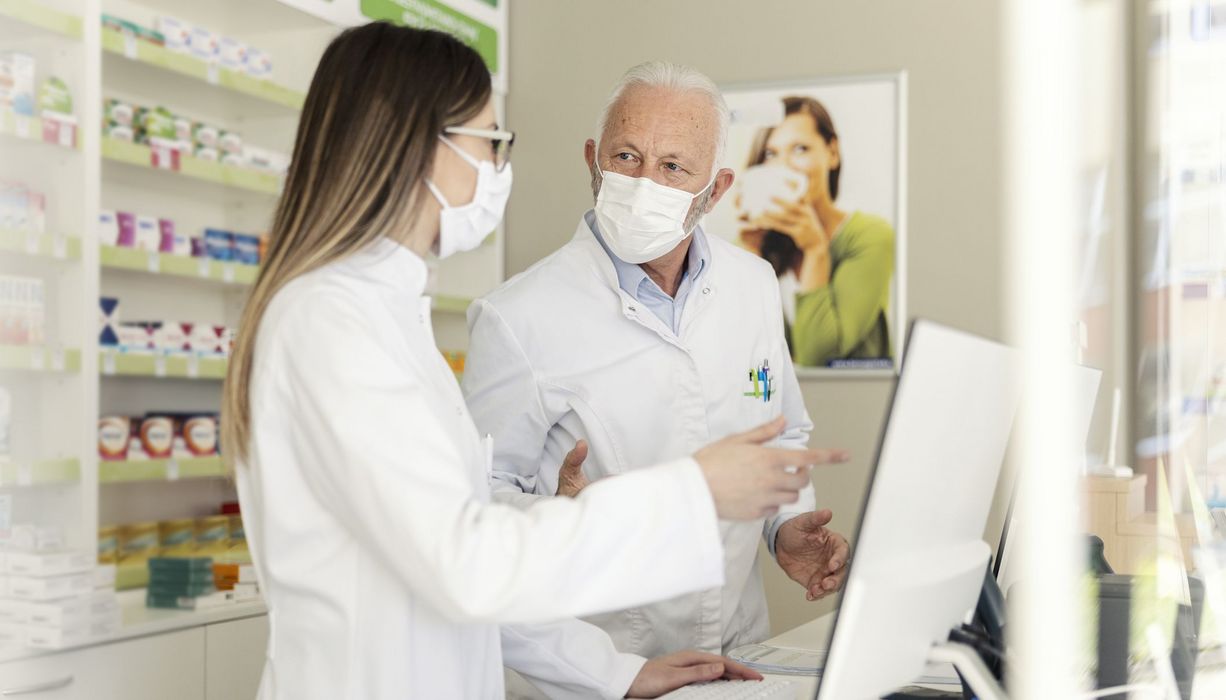 Zwei Apotheker mit Maske vor einem Computer.