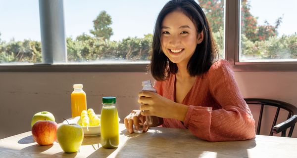 Jugendliches Mädchen sitzt vor Smoothies und Obst.