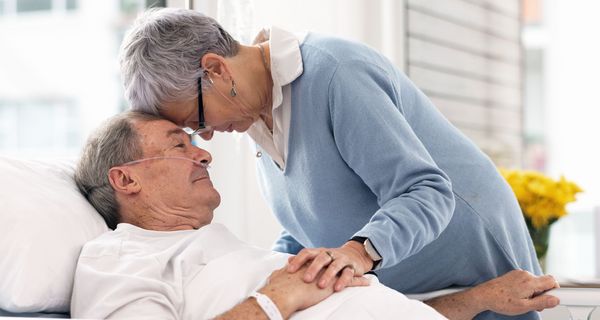 Mann im Krankenhausbett, seine Frau beugt sich über ihn.