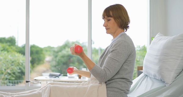 Patientin macht im Krankenbett Übungen mit Hanteln.
