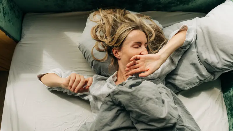 Frau liegt im Bett und gähnt.