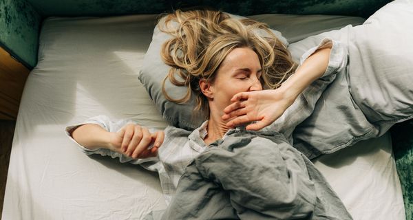 Frau liegt im Bett und gähnt.