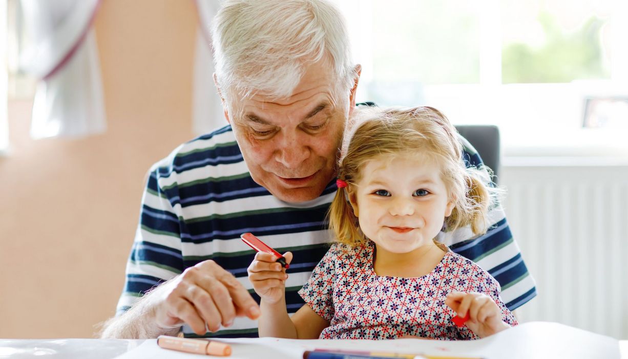 Älterer Mann, zusammen mit Enkeltochter, beide malen ein Bild zusammen.