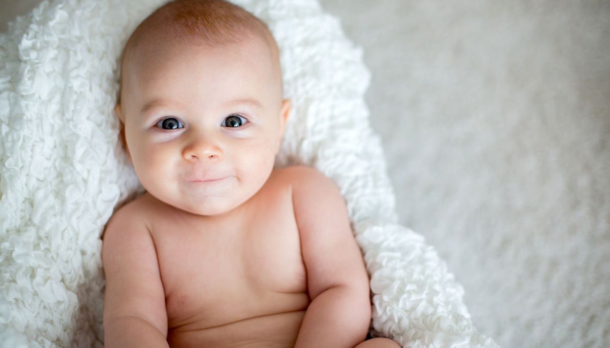 Baby, liegt auf einer weißen Decke und schaut in die Kamera.