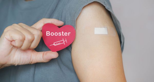 Arm mit Pflaster und einem Herz, auf dem "Booster" steht.