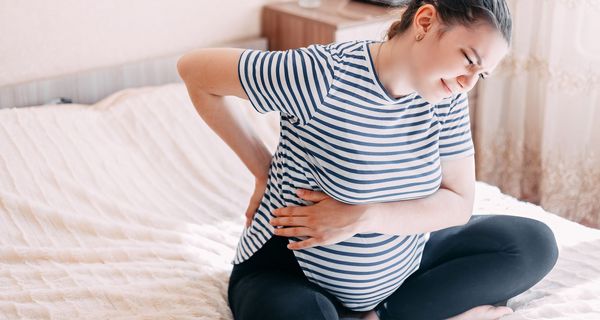 Junge Frau, sitzt auf dem Bett und hat Rückenschmerzen.