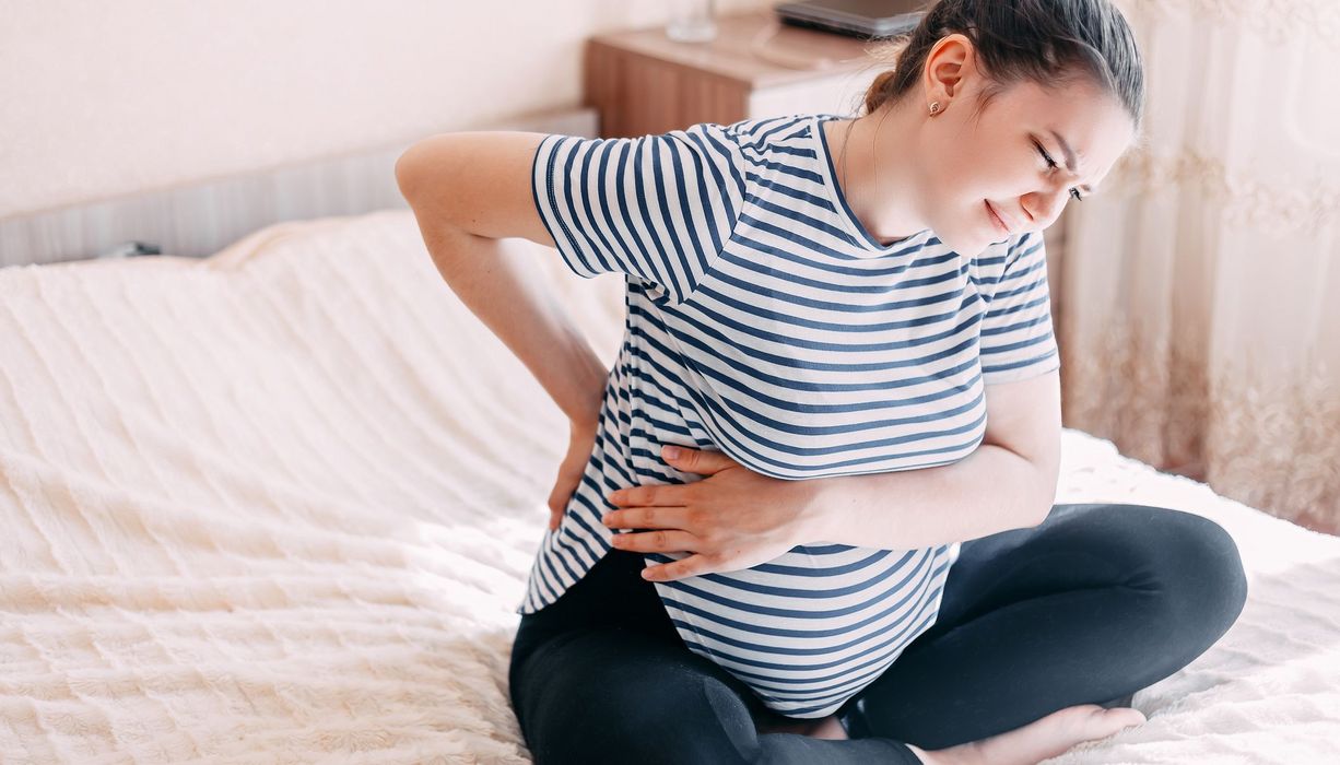 Junge Frau, sitzt auf dem Bett und hat Rückenschmerzen.